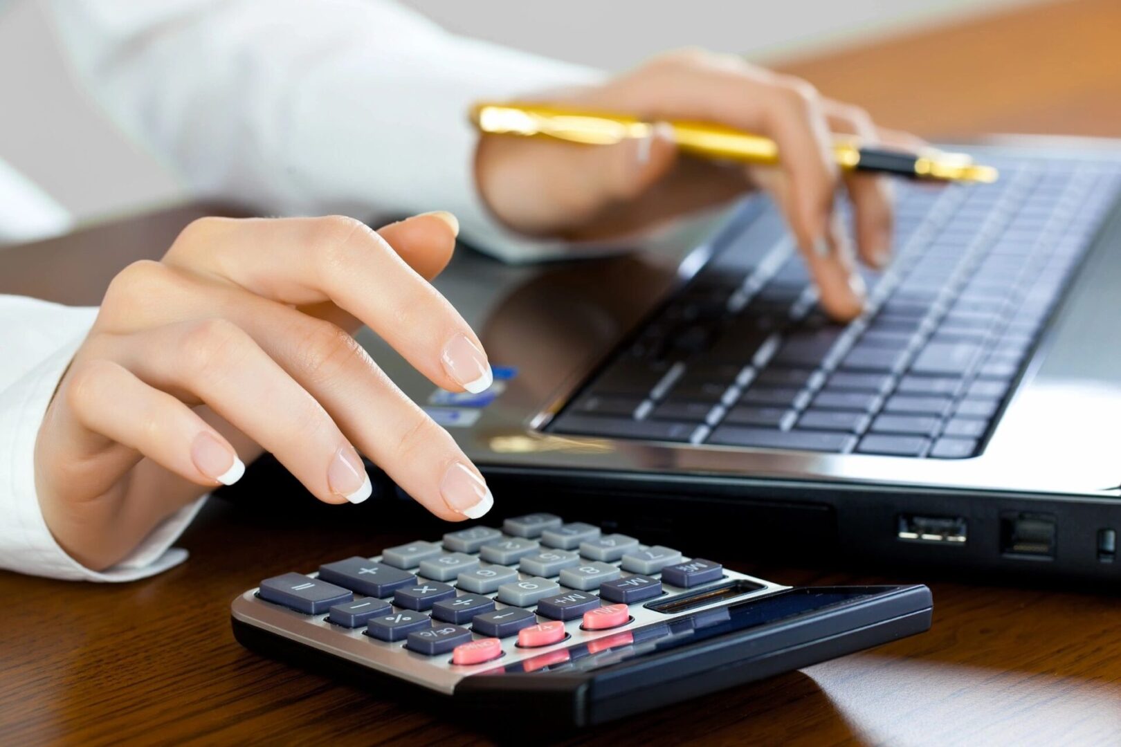 A person using a laptop and calculator on a desk.