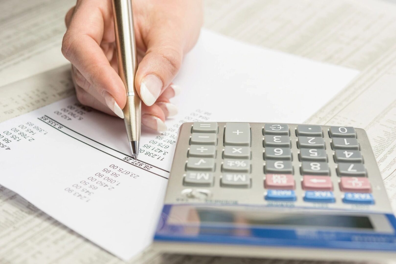 A person writing on top of papers next to a calculator.